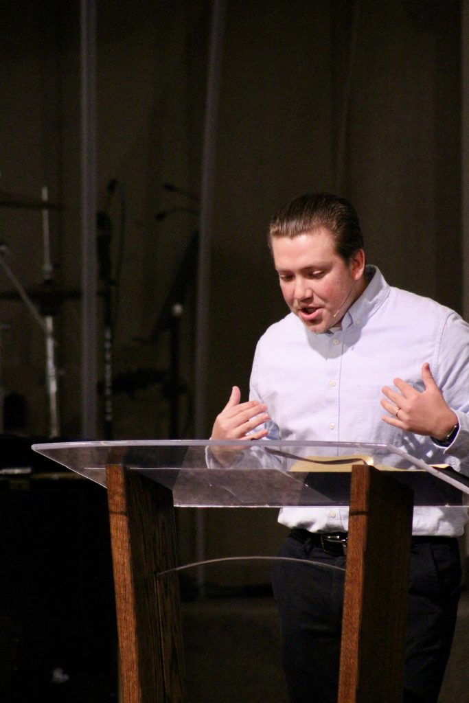 Adam preaching, hands open mid-sentence